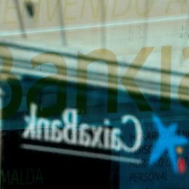 El logo de una oficina de Caixabank se refleja en la ventana de una sucursal de Bankia, en Barcelona. REUTERS/Albert Gea
