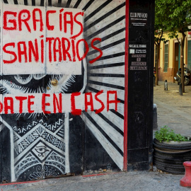 Una mujer con un carro de la compra pasa junto a un comercio cerrado con una pintada de agradecimiento a los sanitarios en una céntrica calle de Sevilla, hoy miércoles en la séptima semana de confinamiento decretado en el Estado de Alarma debido a la c