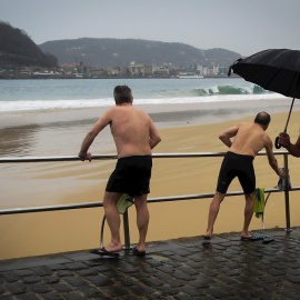 Varios hombres se bañan este martes en la playa de Ondarreta de San Sebastián a pesar del frío y la lluvia. EFE
