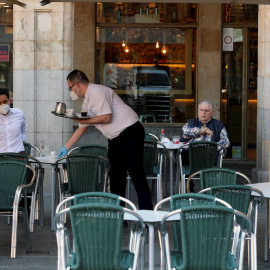 25/05/2020.- Un camarero sirve a los clientes en su bar de la Plaza Mayor de Salamanca este lunes durante el primer día de la fase 1 en la ciudad cuando las terrazas de los bares tienen su capacidad al 50 % y se permite el acceso a los grandes parques. E