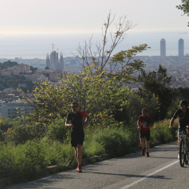 Pla general d'un ciclista i dos corredors pujant pel carrer Manuel Arnús, just abans d'arribar a la carretera de les Aigües, al Parc de Collserola de Barcelona. Imatge del 2 de maig de 2020. (Horitzontal)