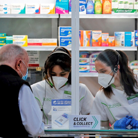 Dos empleadas de una farmacia atienden a un cliente, en una imagen de archivo. / EFE- MANUEL BRUQUE