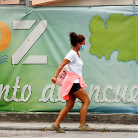 Una mujer con mascarilla camina frente a un cartel publicitario del pueblo de A Mariña, este miércoles en Lugo. | EFE
