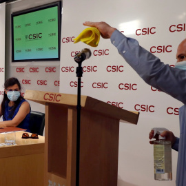 Un asistente desinfecta el micrófono mientras la investigadora Mar Valés (izquierda) da una rueda de prensa, junto al equipo de investigadores, en la sede del Consejo Superior de Investigaciones Científicas (CSIC) en Madrid. EFE/J.J. Guillén