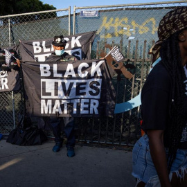 Un hombre (L) con una máscara facial vende banderas y otros accesorios con el eslogan 'Black Lives Matter'