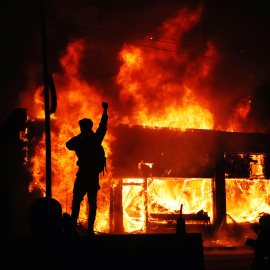 Un manifestante delante de una edificio ardiendo durante los disturbios desatados en Minesota tras la muerte de George Floyd, un ciudadano negro, a manos de la policía.- REUTERS