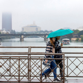 17/11/2019.- Dos personas atraviesan el puente de San Telmo en un día de lluvia en Sevilla. / EFE - JULIO MUÑOZ