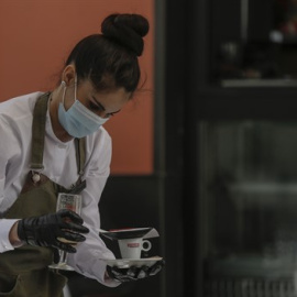 Una camarera con mascarilla y guantes atiende un bar de la capital hispalense durante el quinto de la Fase 1 del plan de descalada que ha elaborado el Gobierno de España. En Sevilla (Andalucía, España)