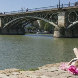 Una mujer toma el sol a orillas del Guadalquivir, bajo el Puente de Triana en Sevilla / EFE (RAÚL CARO)