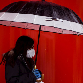 Una mujer camina bajo la lluvia con mascarilla y guantes en Málaga, durante la novena jornada de confinamiento tras decretarse el Estado de Alarma. EFE/Jorge Zapata