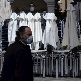 Un hombre ataviado con una mascarilla pasa por delante de una terraza recogida de un bar | EFE
