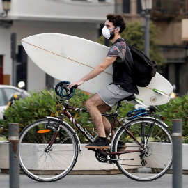 Un surfista protegido con mascariilla carga su tabla en bici hacia la playa de la Malvarrosa, en Valencia, hoy quincuagésimo sexto día del estado de alarma. EFE/ Juan Carlos Cárdenas