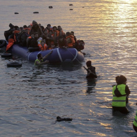 Voluntarios de una ONG ayudan a refugiados y migrantes que llegan en una lancha neumática a la costa de Mytilini, en la isla de Lesbos (Orestis Panagiotou / EFE)