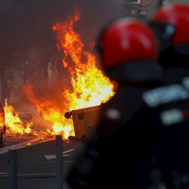 , 03/07/2020.- Agentes de la Ertzaintza observan un contenedor ardiendo en las calles de San Sebastián, donde la formación política Vox celebra esta tarde un acto electoral. EFE/Juan Herrero