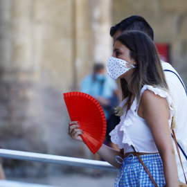 Una mujer protegida con unas mascarilla mientras se abanica para aliviar las altas temperaturas de este jueves en Córdoba. | EFE