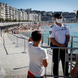 Un agente de la Policía Municipal impide el acceso este miércoles a la playa de La Concha de San Sebastián, coincidiendo con la pleamar, para evitar un exceso de aforo. EFE/Javier Etxezarreta