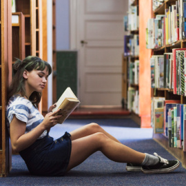 Chica leyendo en una biblioteca.- Freepik