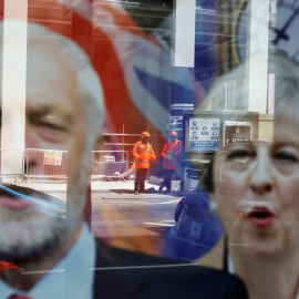 Trabajadores instalando vallas de seguridad se reflejan en el escaparate de una tienda con imágenes de la Primera Ministra británica Theresa May y el candidato laborista Jeremy Corbyn en Londres. REUTERS/Marko Djuric