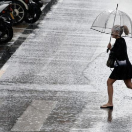 Una mujer cruza un paso de cebra bajo la lluvia. EFE/Archivo.