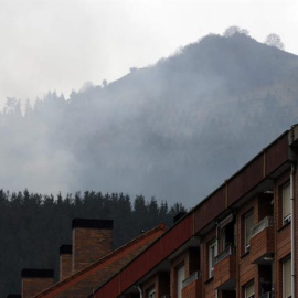 Viviendas en la localidad vizcaína de Ermua, con el fuego de fondo, donde este viernes el Gobierno Vasco ha decidido reactivar las medidas preventivas de no ventilar las casas y de no hacer deporte al aire libre en el barrio de San Lorenzo de Ermua (Bizk