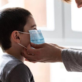 Una madre coloca a su hijo una mascarilla. / EFE