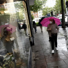 Una mujer pasa frente a una tienda con un paraguas un día de lluvia y bajada de temperaturas en toda España. Óscar Cañas / Europa Press / Archivo