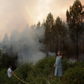 Dos habitantes de Louriceira intentan apagar un foco cerca de su pueblo. | MIGUEL VIDAL (EFE)