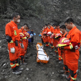 Trabajadores de rescate chinos rinden un minuto de silencio ante el cuerpo de una de las victimas del alud que sepultó una aldea del Tibet./REUTERS
