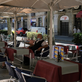 Un camarero, con mascarilla, espera sentado en una mesa la llegada de clientes a la terraza de un bar en las Ramblas de Barcelona. REUTERS/Nacho Doce