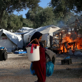 Una mujer trata de recuperar alguna de sus pertenencias, mientras el fuego sigue consumiendo las carpas del campamento de refugiados de Moria. - EFE
