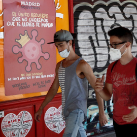 MADRID, 04/08/2020.- Dos jóvenes pasan ante un cartel alusivo al coronavirus en el centro de Madrid, este martes 4 de agosto, EFE/Mariscal