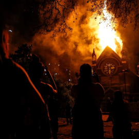 Un grupo de manifestantes observa como arde la iglesia de San Francisco de Borja, actualmente destinada al servicio religioso de Carabineros de Chile, este domingo durante una manifestación en los alrededores de la Plaza Italia de Santiago (Chile), rebau