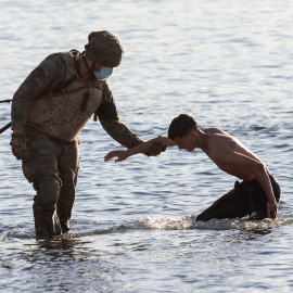 Un soldado del ejército ayuda a un migrante a su llegada a la playa de El Tarajal. — EFE