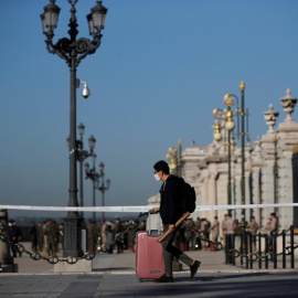 Un joven con su maleta pasa ante el Palacio Real de Madrid.