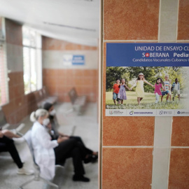 Imagen de archivo de varias personas sentadas cerca de un cartel que anuncia los ensayos clínicos de la vacuna Soberana 02, en una clínica sanitaria en La Habana. - REUTERS
