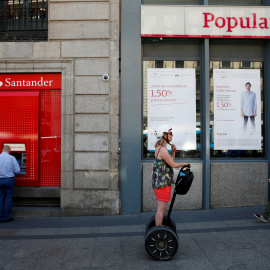 Un hombre utiliza un cajero automático del Banco Santander junto a una oficina del Popular, en Madrid. /Juan Medina