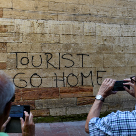 Dos personas toman una foto de una pintada contra el turismo en el centro histórico de Oviedo. REUTERS/Eloy Alonso