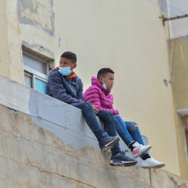 Dos niños sentados sobre un muro en la nave de primera acogida del polígono del Tarajal, a 20 de mayo de 2021, en Ceuta (España).- Antonio Sempere / Europa Press