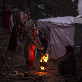 Una refugiada se calienta en un fuego en el campo de acogida de Samos.