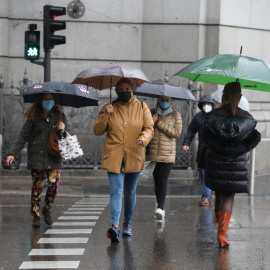 Transeúntes caminan por el centro de la capital protegiéndose de la lluvia con paraguas, en Madrid.