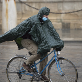 Un hombre circula en bicicleta protegido de la lluvia con un impermeable.