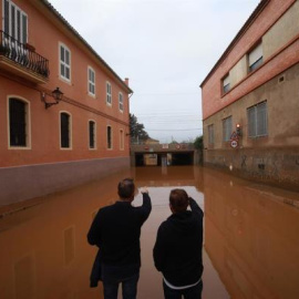 Dos hombres observan el acceso a un paso inferior de la vía ferroviaria inundado por el temporal que afectó en la localidad valenciana de Carcaixent.
