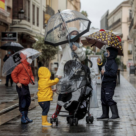 Una mujer con tres menores se protegen de la lluvia con paraguas y chubasqueros en una céntrica calle de València.