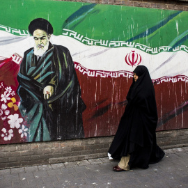 Una mujer junto a un mural con la bandera iraní y el ayatolá Ruholá Jomeini en Teherán (Irán). Imagen de Archivo.