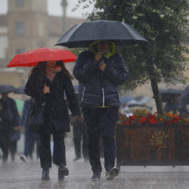 Unas personas se protegen con paraguas de la lluvia mientras caminan por el puente romano de Córdoba en una jornada en la que la ciudad se encuentra en aviso amarillo por lluvias.