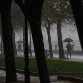 Algunos paseantes se protegen con paraguas de un fuerte chaparrón caído en San Sebastián.
