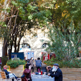 Varias personas almuerzan en un banco de una calle del centro de Barcelona