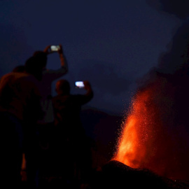 Cuatro personas contemplan desde una montaña al caer la noche la lava que sale del volcán de La Palma este lunes 20 de septiembre de 2021.