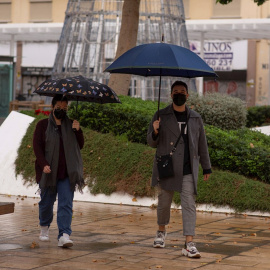Dos personas se protegen de las lluvia bajo sus paraguas en Málaga.