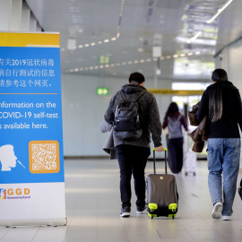 Viajeros de China pasan frente a una pancarta con información y reciben un test de covid-19 a su llegada a Schiphol, Países Bajos, el 04 de enero de 2023.